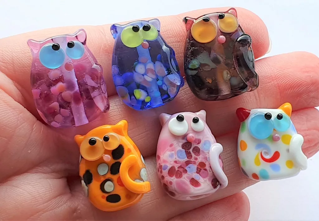 A collection of lampwork glass beads resembling cats, with frit, dots and swirls. 