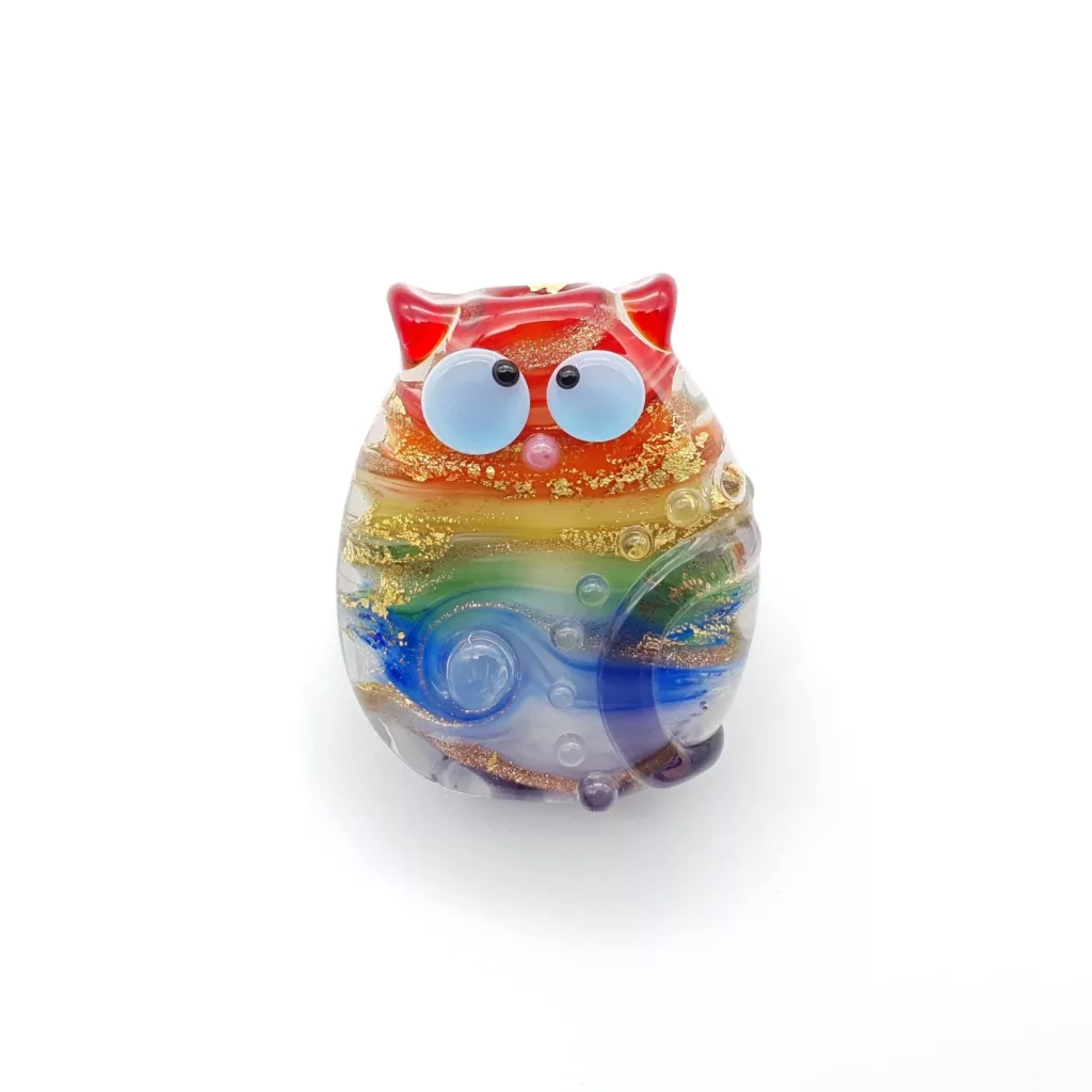 Lampwork glass bead cat in rainbow streaks, with kooky eyes and dots. Decorated with gold.