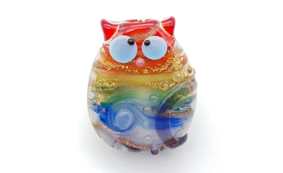 Lampwork glass bead cat in rainbow streaks, with kooky eyes and dots. Decorated with gold.