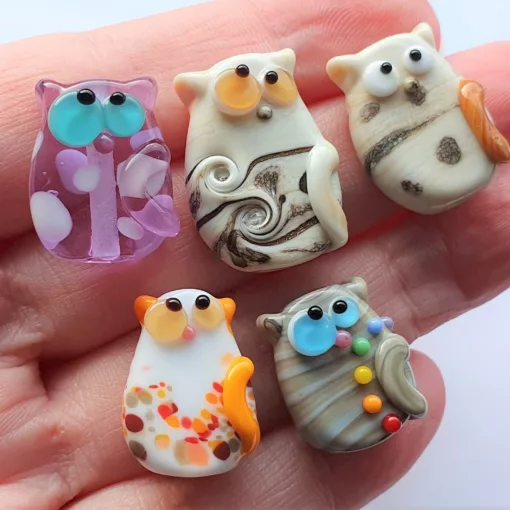 A collection of lampwork glass beads resembling cats of various colors and styles.