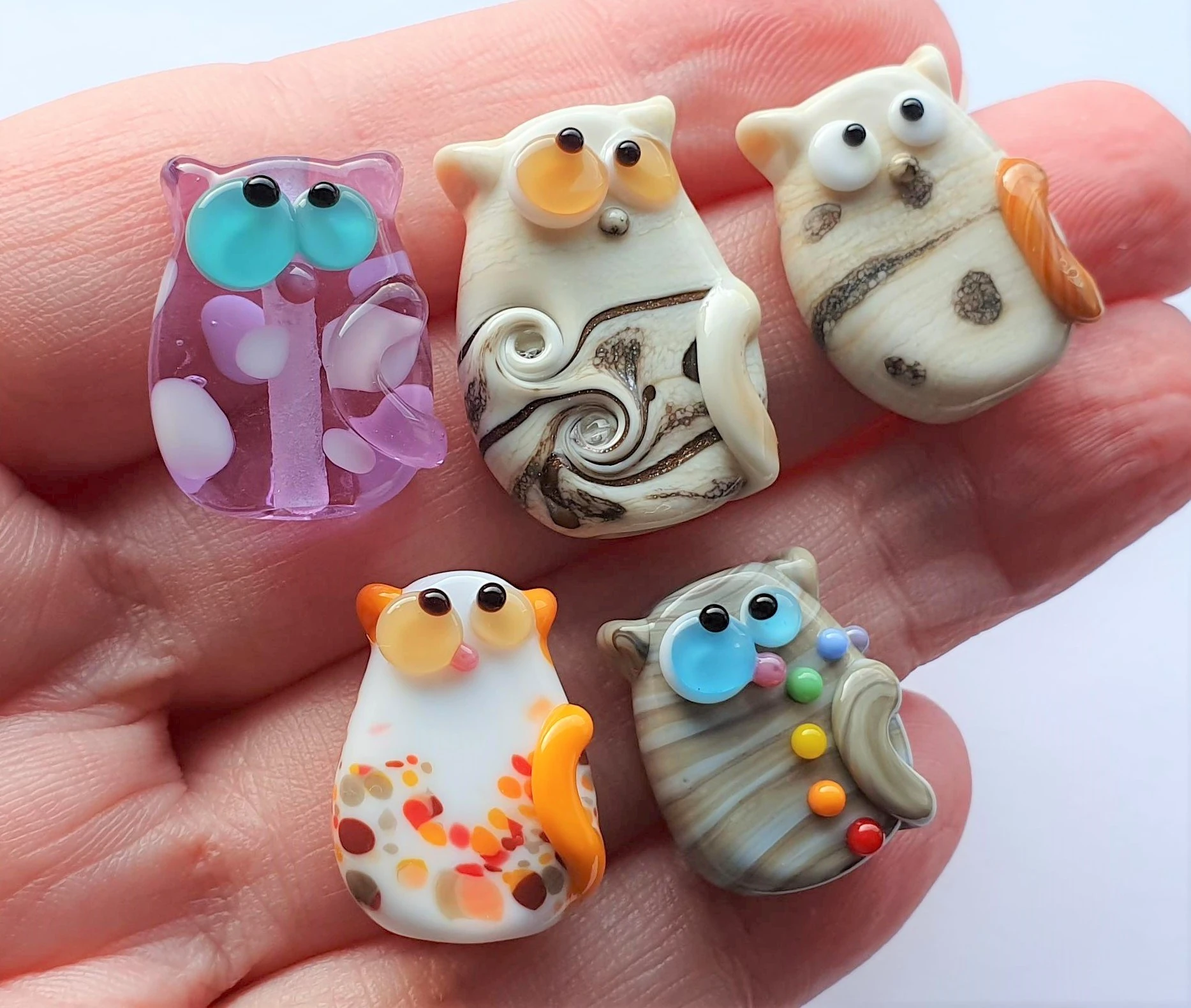 A collection of lampwork glass beads resembling cats of various colors and styles.